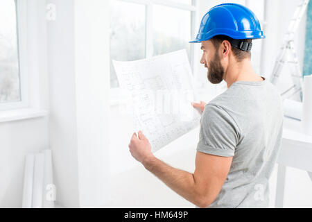 Handsome repairman or builder in helmet working with drawings on renovation of interior Stock Photo