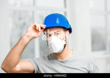 Portrait of a builder or repairman in protective helmet and facial mask indoors Stock Photo