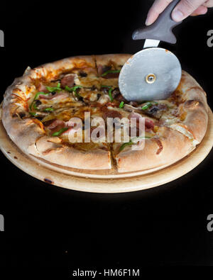 Wheel cutter slicing pizza black background Stock Photo