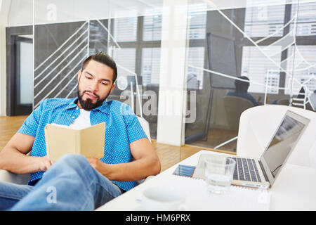 Student as programmer with computer reading book in office Stock Photo
