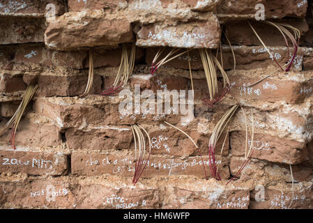 Mingun Pahtodawgyi Unfinished Pagoda Incense Sticks In Brick Wall Mingun Myanmar // MINGUN, Myanmar — Incense sticks burned by devotees are pressed into the gaps between bricks along the wall of the Mingun Pahtodawgyi, also known as the Unfinished Pagoda of Mingun. This massive solid brick structure was commissioned by King Bodawpaya in 1790 and intended to reach 492 feet (150 m), though it stands unfinished at 164 feet (50 m). An earthquake in March 1839 tore large cracks through the edifice. The pagoda stands in Mingun, Sagaing Region, and remains an active site of devotion as well as a majo Stock Photo