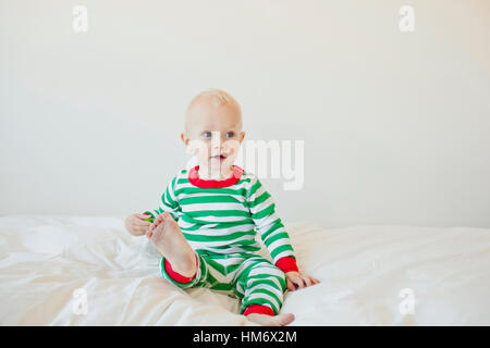 Cute baby boy looking away while sitting on bed against white background Stock Photo