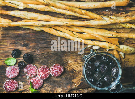 Grissini bread sticks, sausage, black olives on wooden background Stock Photo