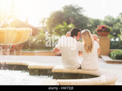Happy family with two baby girls (2-5 months) near fountain in sunlight Stock Photo