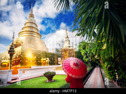 Woman tourist with red traditional Thai umbrella near Golden Stupa at temple Wat Phra Singh in Chiang Mai, Thailand Stock Photo