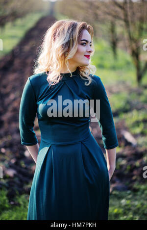 Yong elegance blonde girl at green dress on the garden in spring. Stock Photo