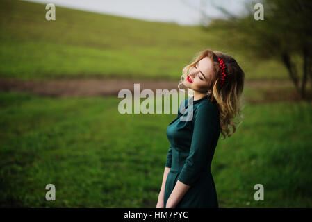 Yong elegance blonde girl at green dress on the garden in spring. Stock Photo