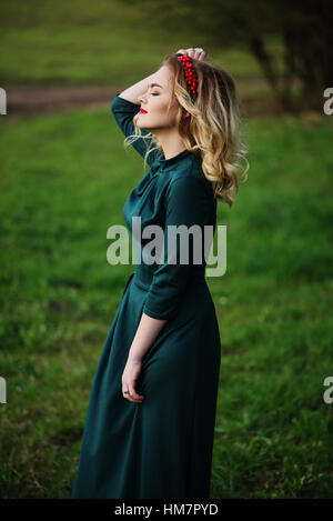 Yong elegance blonde girl at green dress on the garden in spring. Stock Photo