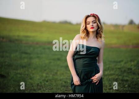 Yong elegance blonde girl at green dress on the garden in spring. Stock Photo