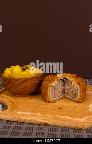 Piccalilli relish in a wooden bowl on a board. Stock Photo