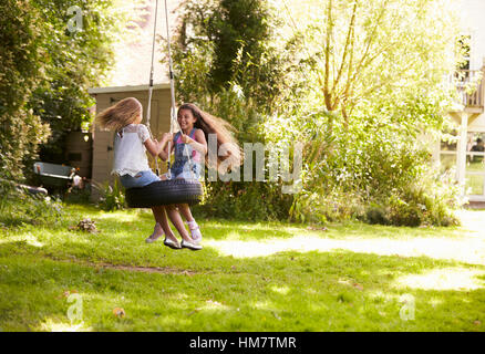 Two Girls Playing Together On Tire Swing In Garden Stock Photo