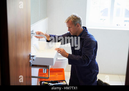 Plumber Mending Sink Tap In Bathroom Stock Photo
