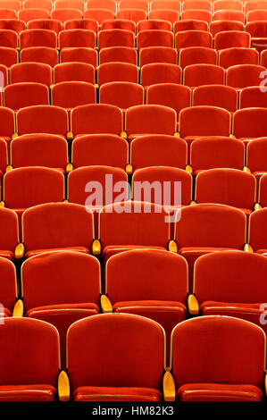 Empty theater seats in vibrant red with wooden arm rests, a concert hall stage view of no audience or patrons, old style seating Stock Photo