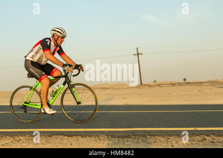 DUBAI, UAE - NOVEMBER 7, 2016: Cyclist on a bicycle in the desert. Asphalt bicycle path in the desert, the road divide tree in the middle. Sport in th Stock Photo