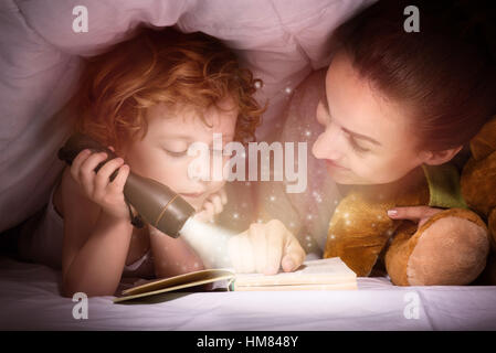 Delighted mother and son enjoying book before sleeping Stock Photo