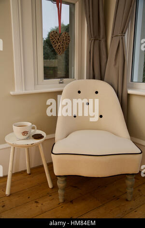 Traditional victorian cream chair in corner by window at home with table with cup of tea and biscuit ready to take a break relax Stock Photo