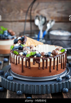 Delicious three chocolate mousse cake decorated with waffle cone, fresh blueberry, mint, candies and frosting Stock Photo