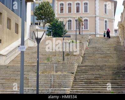 Woman wearing head scarf, carrying shopping bag and holding hands with small boy, descending very high set of stone steps, Marseille, France Stock Photo