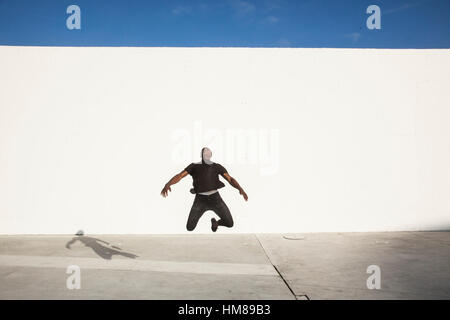 Young Adult Man Jumping in Air with Large White Wall in Background Stock Photo