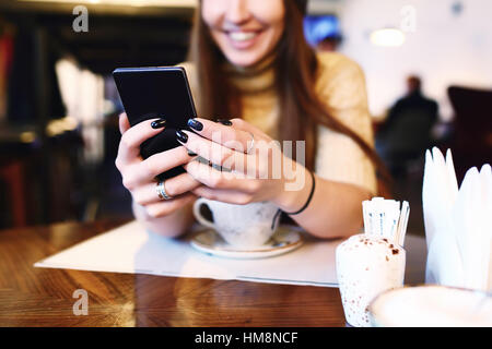 Close up of women's hands holding cell telephone with blank copy space scree for your advertising text message or promotional content, hipster girl watching video on mobile phone during coffee break. Tonned. Selective focus. Stock Photo
