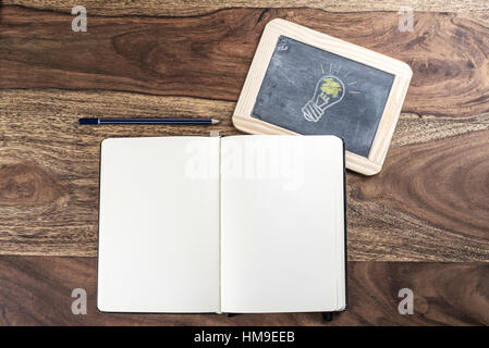 open plain empty page notebook with pencil and light bulb on blackboard on rustic wood table Stock Photo