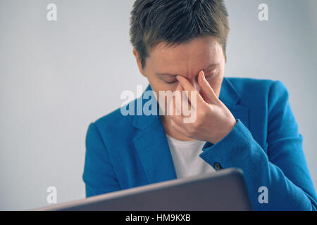 Exhausted businesswoman working overtime on office laptop computer, hand on the forehead Stock Photo