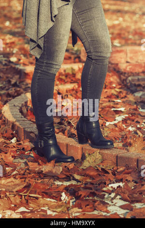 Woman's legs in black jeans and black high heel boots standing in the park in fallen leaves Stock Photo