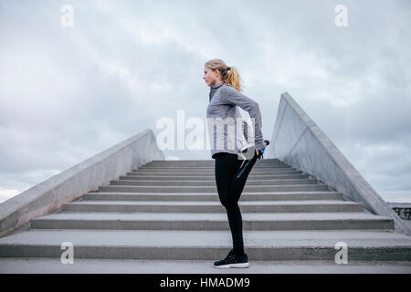 Side view of young female stretching her leg. Fitness woman warming up before jogging. Stock Photo