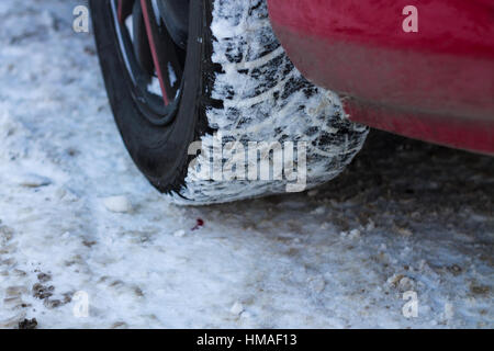 Modern red car fragment, wheel with studded tire standing on winter road with dirty snow, close up photo with selective focus Stock Photo