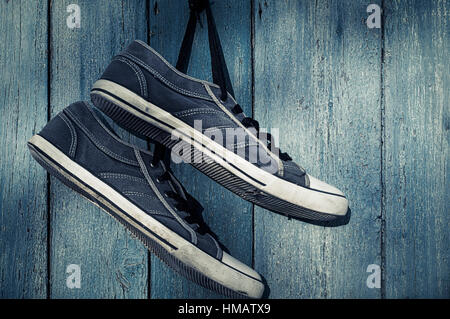 Blue textile torn sneakers hanging from a nail on a background of blue wooden wall Stock Photo