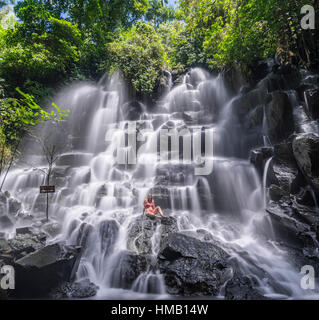 Woman sitting on rock, waterfall, Air Terjun Kanto Lampo, near Ubud, Bali, Indonesia Stock Photo