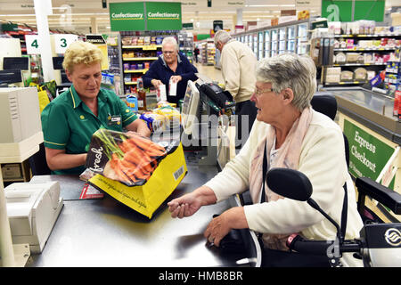 A disabled woman is helped at the supermarket checkout with her shopping, bag packing. Stock Photo