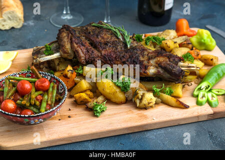 Roast lamb shoulder with roasted potatoes and carrots styled in a rustic wooden board, top view Stock Photo