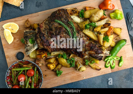 Roast shoulder of lamb on baked potato and carrots, wooden board, top view Stock Photo