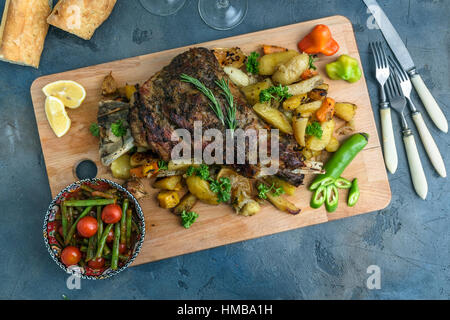 Roast shoulder of lamb on baked potato and carrots, wooden board, top view Stock Photo