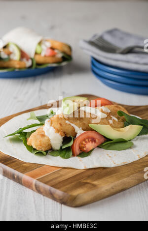 Fish finger wraps with avocado and tomato serves on wooden cheese platter Stock Photo