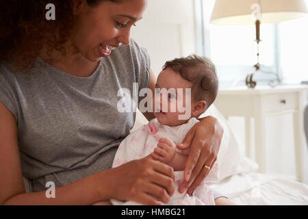 Mother Cuddling Baby Daughter In Bedroom At Home Stock Photo