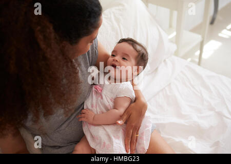 Mother Cuddling Baby Daughter In Bedroom At Home Stock Photo