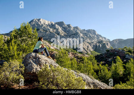 Woman, hiker seated on a rock in front of the mountain 'montagne Sainte-Victoire' (south-eastern France). Stock Photo