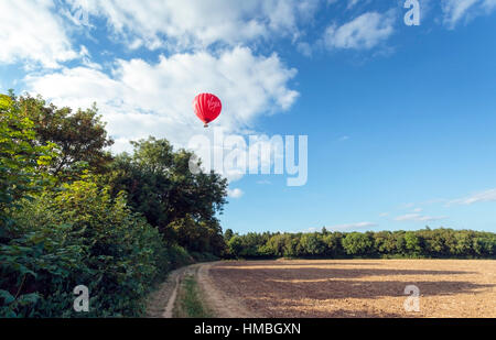 Virgin hot air balloon drifts over newly ploughed farm field and trees in the Chilterns on a summer evening Stock Photo