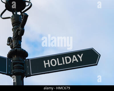 Street lighting pole with conceptual message HOLIDAY on directional arrow over blue cloudy background. Stock Photo