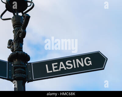 Street lighting pole with conceptual message LEASING on directional arrow over blue cloudy background. Stock Photo