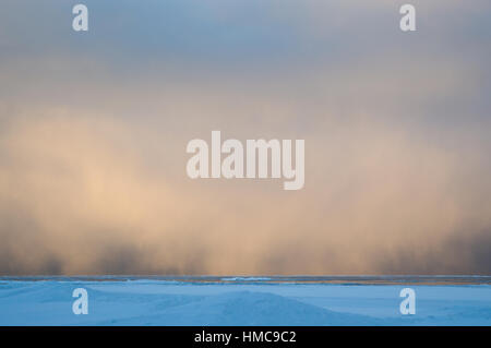 Sidelit snow squall clouds rolling in across the frozen Lake Huron at sunrise.  Ice floats on the still calm water. Stock Photo