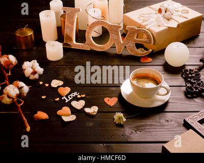 Valentine's day composition of wood crafted word love, cup of coffee, present and candles on wooden table Stock Photo