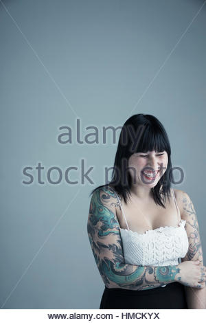 Portrait enthusiastic brunette mixed race young woman with arm tattoos laughing with eyes closed