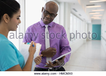 Male doctor and female nurse with medical chart consulting, using digital tablet in clinic corridor