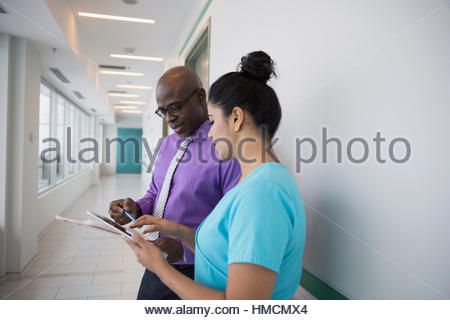 Male doctor and female nurse consulting, using digital tablet in clinic corridor
