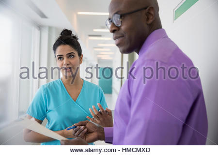 Male doctor and female nurse consulting, discussing medical chart in clinic corridor