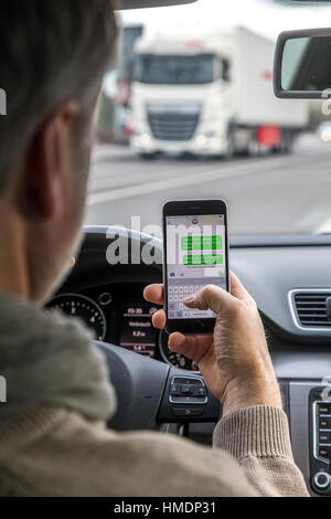A car driver is using a mobile phone, smartphone, while driving the car, writing a SMS message, Stock Photo