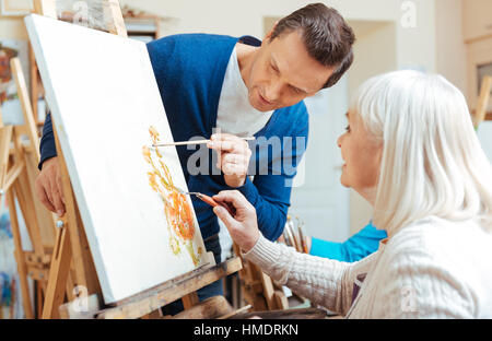 Serious artist helping elderly woman in painting school Stock Photo